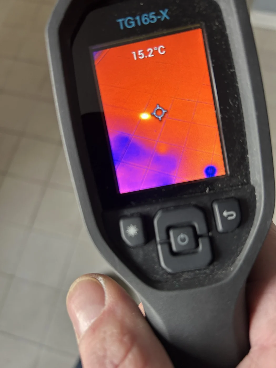 Thermal camera screen showing a concentrated bright hot spot on a tiled floor