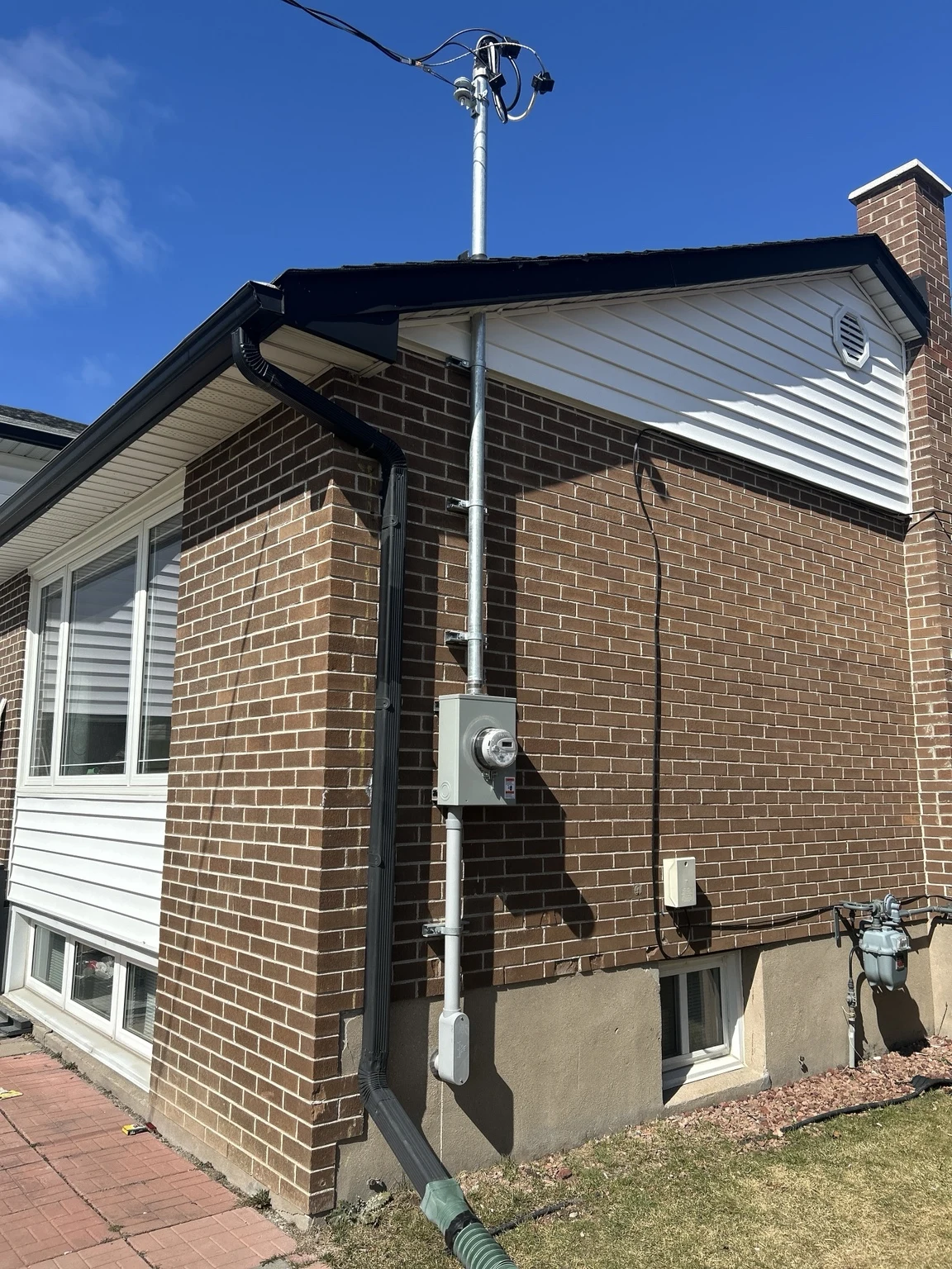 Exterior electrical meter and overhead service mast on a brick home, shown from the weatherhead to the lower conduit