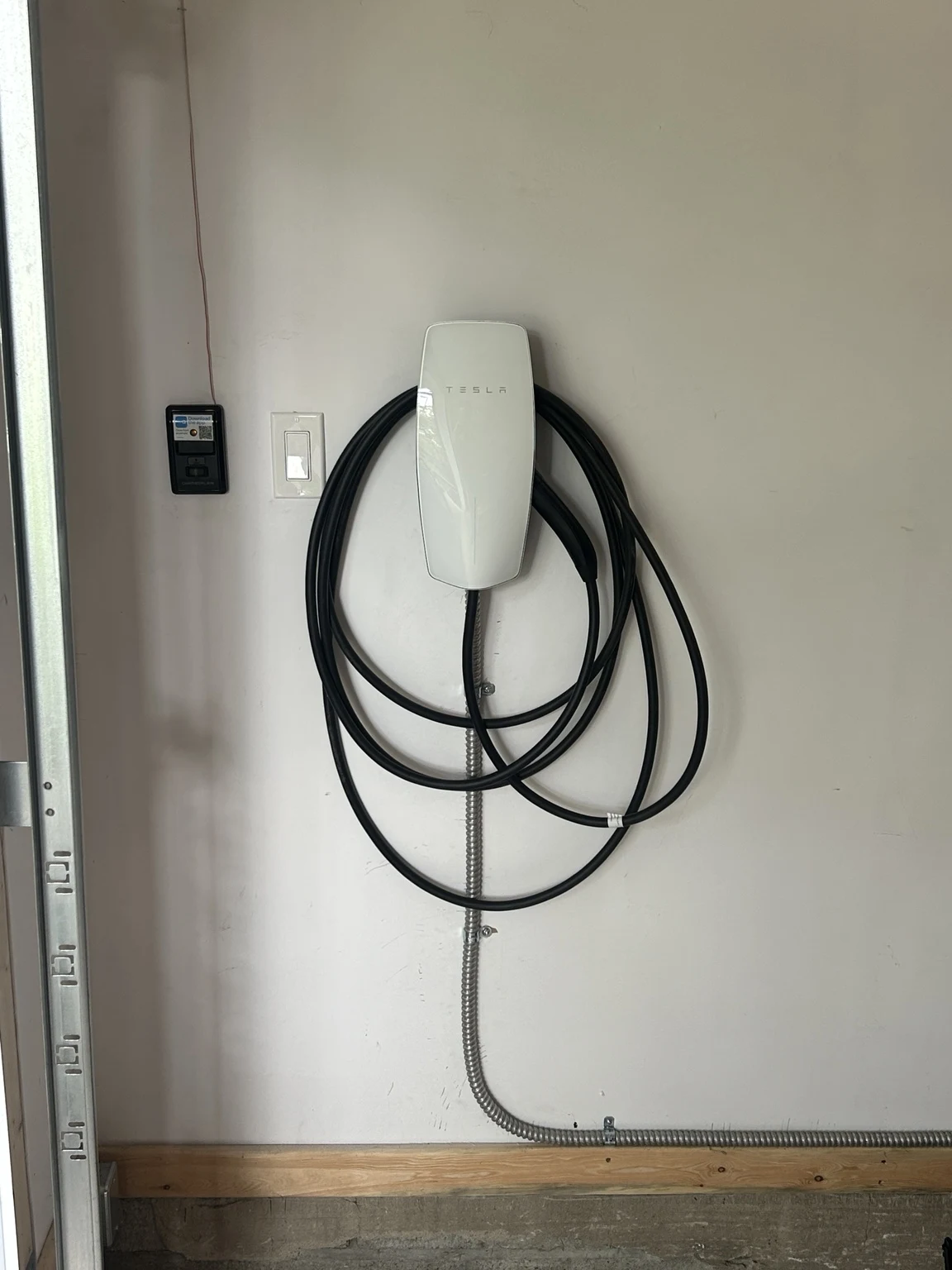 Completed Tesla Wall Connector installation in a garage, with charging cable and surface mounted supply cable