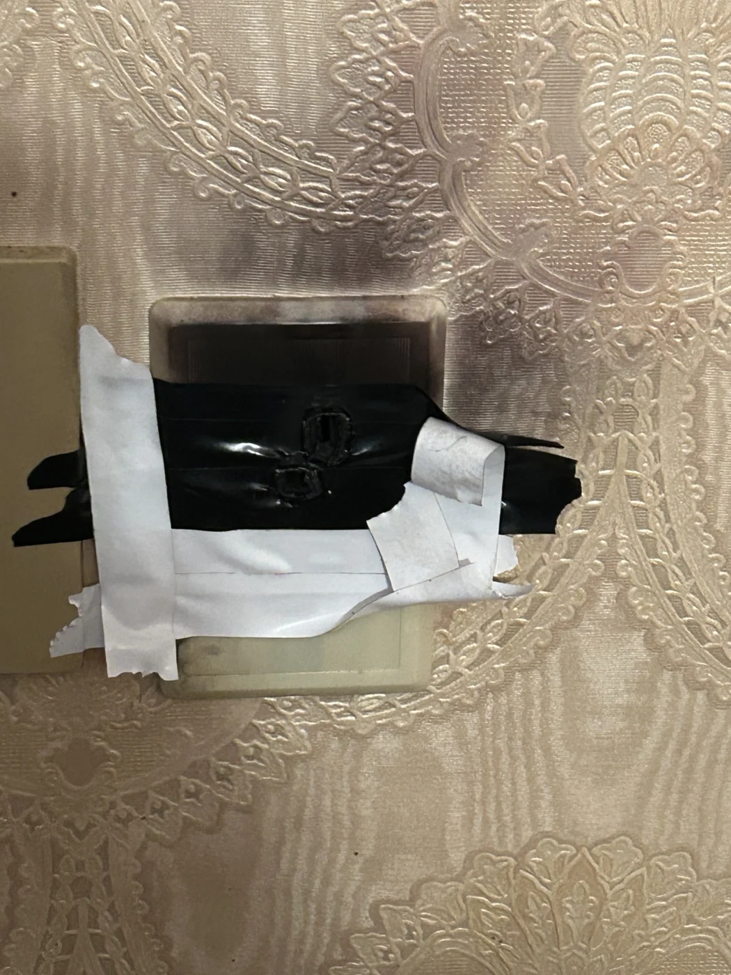 Outlet covered with tape with dark marks on the surrounding wallpaper